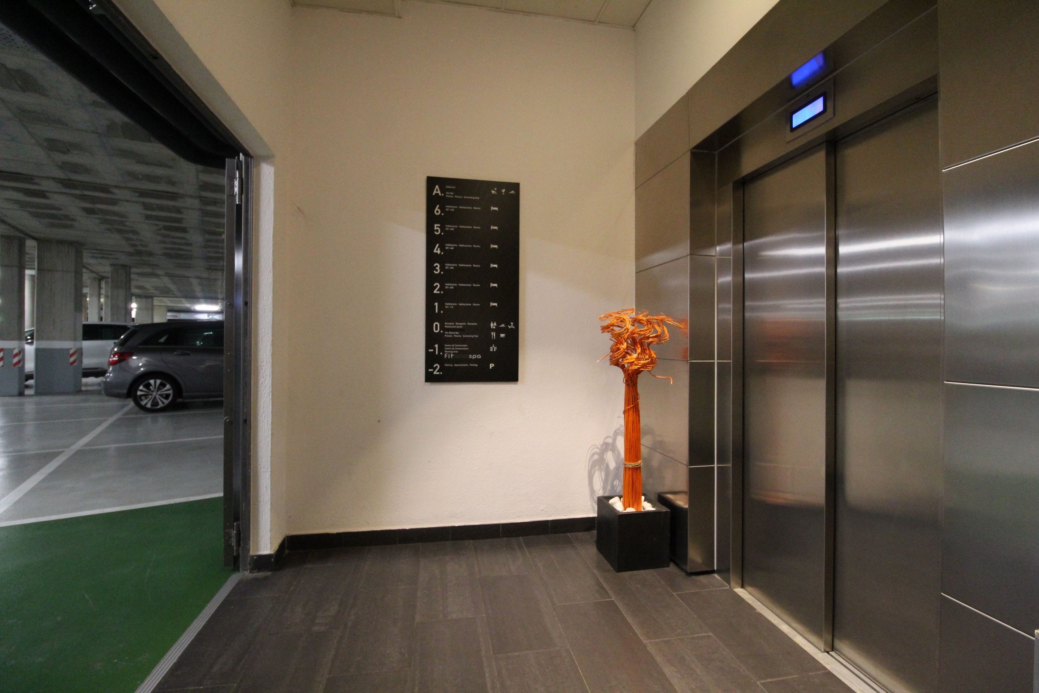 An elevator with a digital display, a directional sign, and a sculpture in the lobby.