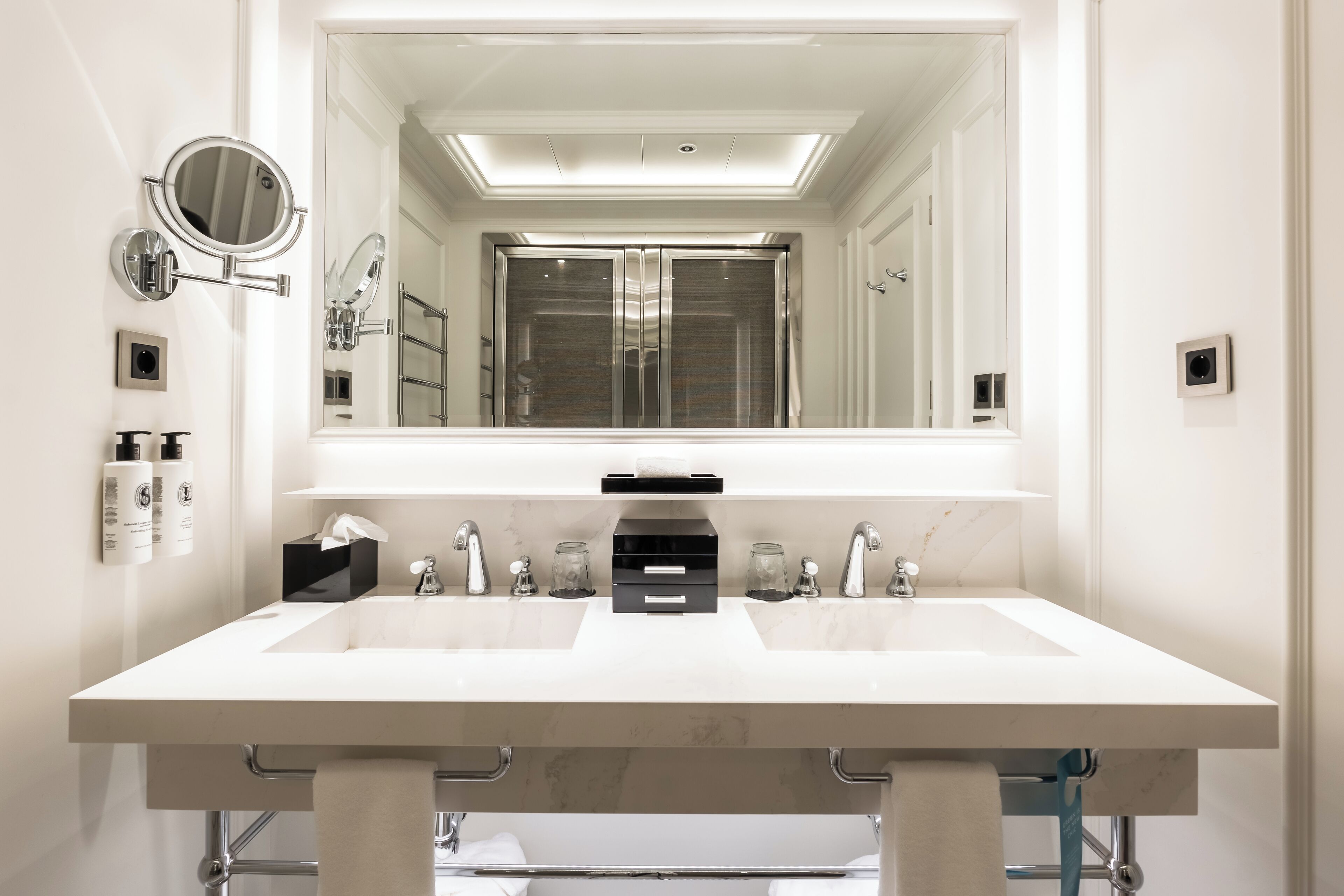 A modern bathroom with a large mirror, two sinks, and a towel rack.