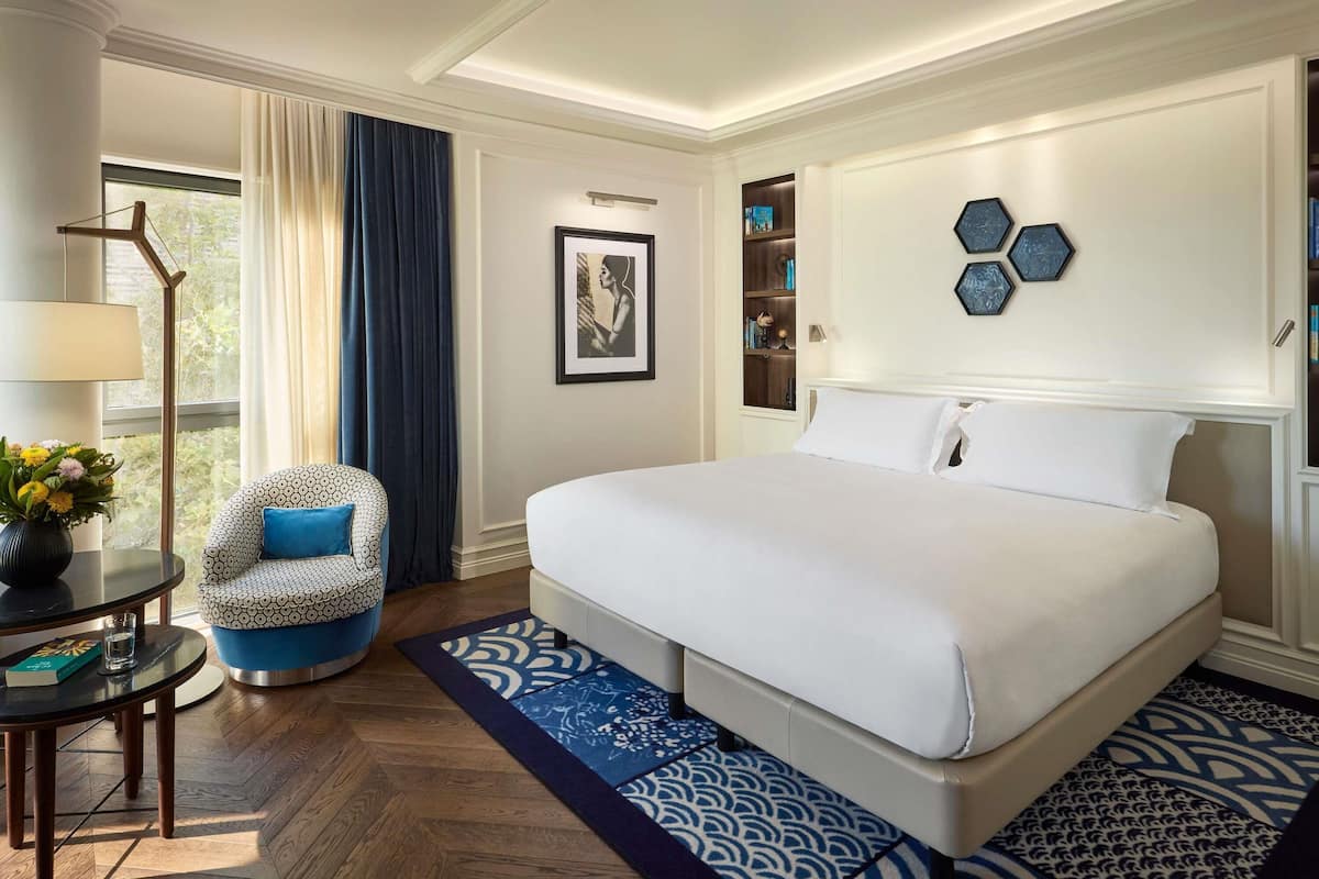 Ein Hotelzimmer mit einem großen Bett, einem Sessel, einem kleinen Tisch und einem Bücherregal.