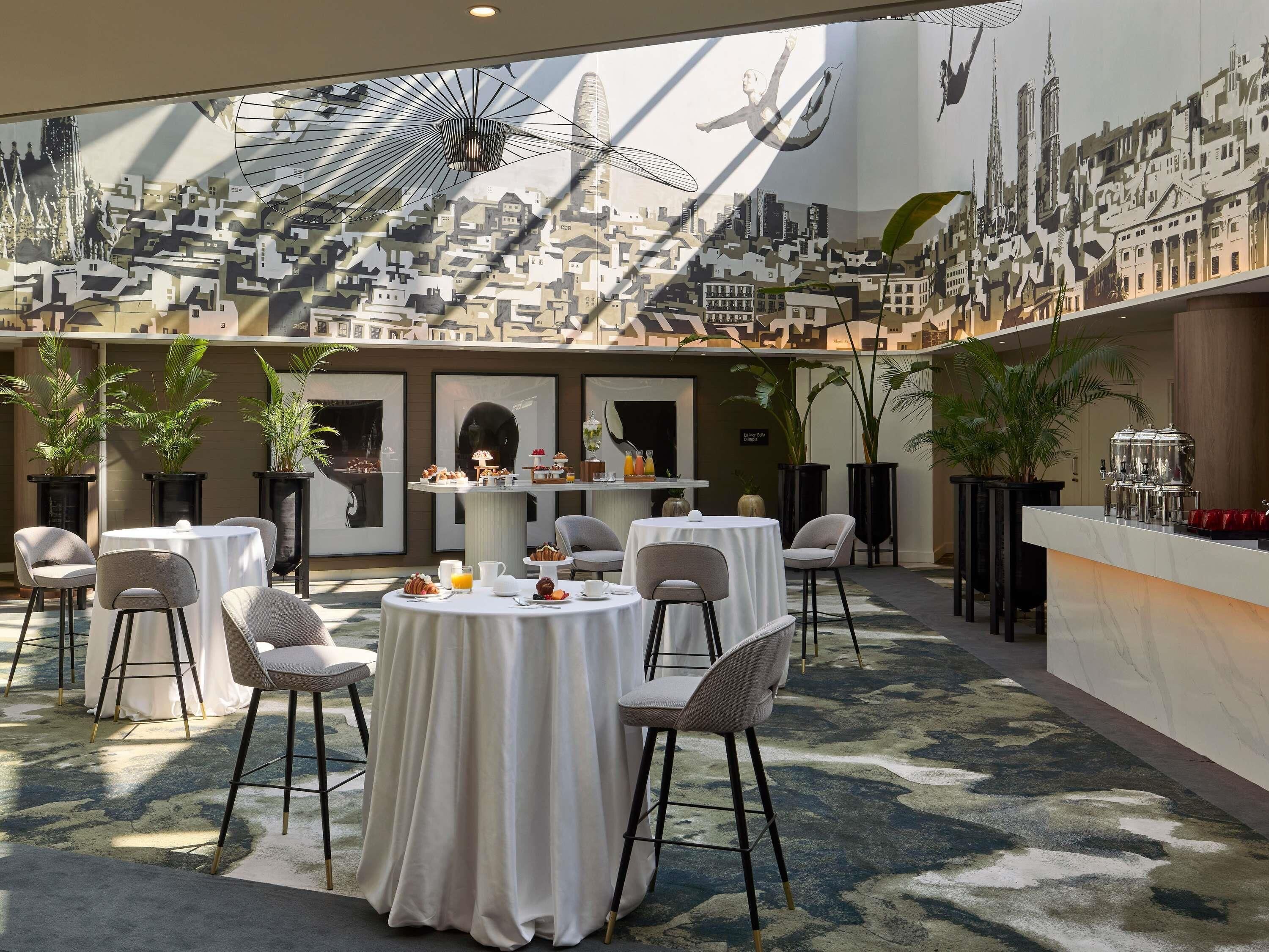 Un comedor con mesas redondas, sillas y un mural con vistas a la ciudad.