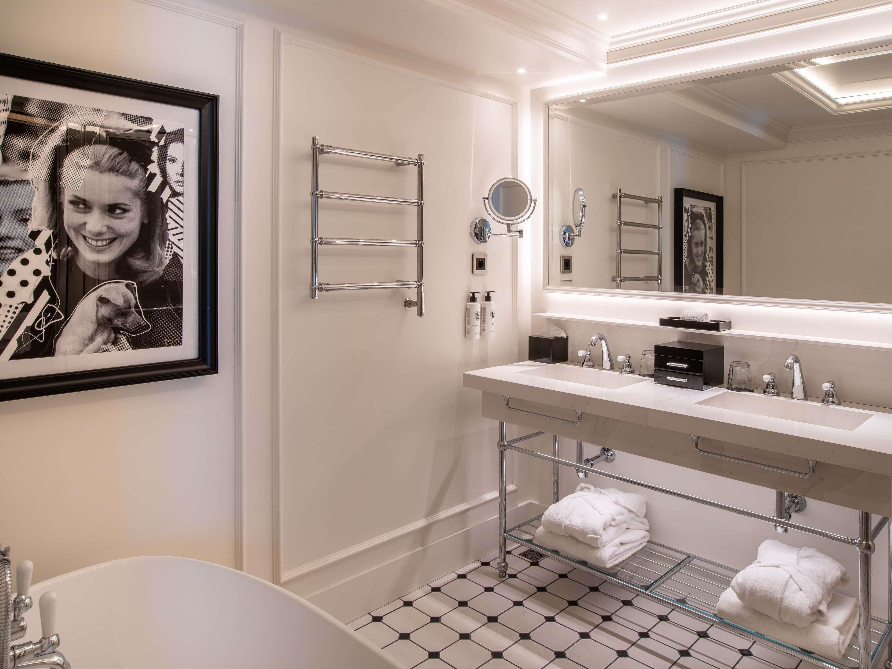 Un baño moderno con bañera, dos lavamanos, un espejo grande, toalleros y un cuadro enmarcado en la pared.
