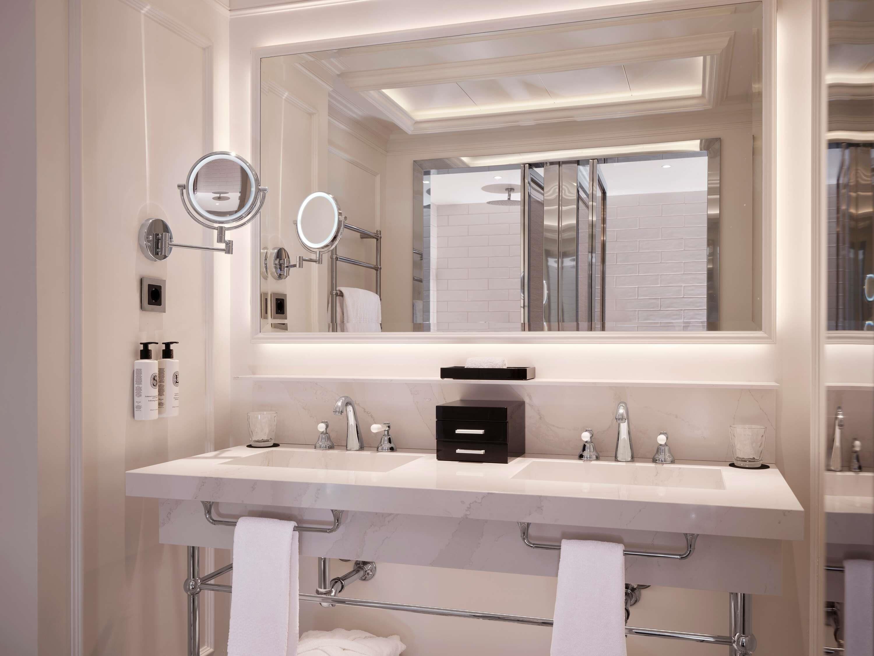 A modern bathroom with two sinks, a large mirror, and a towel rack.