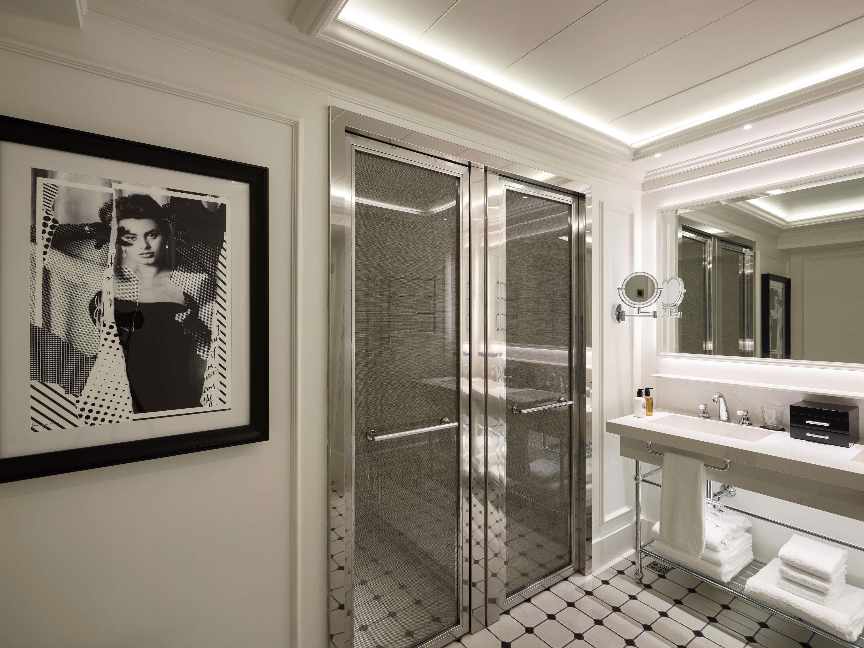Une salle de bain moderne avec une douche à parois de verre, un lavabo blanc avec un miroir et une œuvre d’art encadrée accrochée au mur.