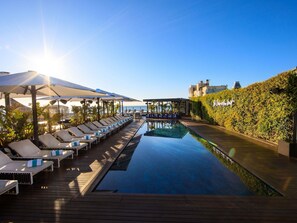 Uma piscina infinita no terraço, com espreguiçadeiras, um deck de madeira e vista para o oceano.