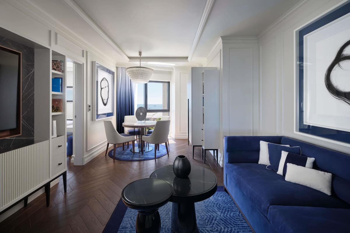 Ein modernes Wohnzimmer mit einem blauen Sofa, einem Essbereich mit rundem Tisch und Blick durch ein großes Fenster.