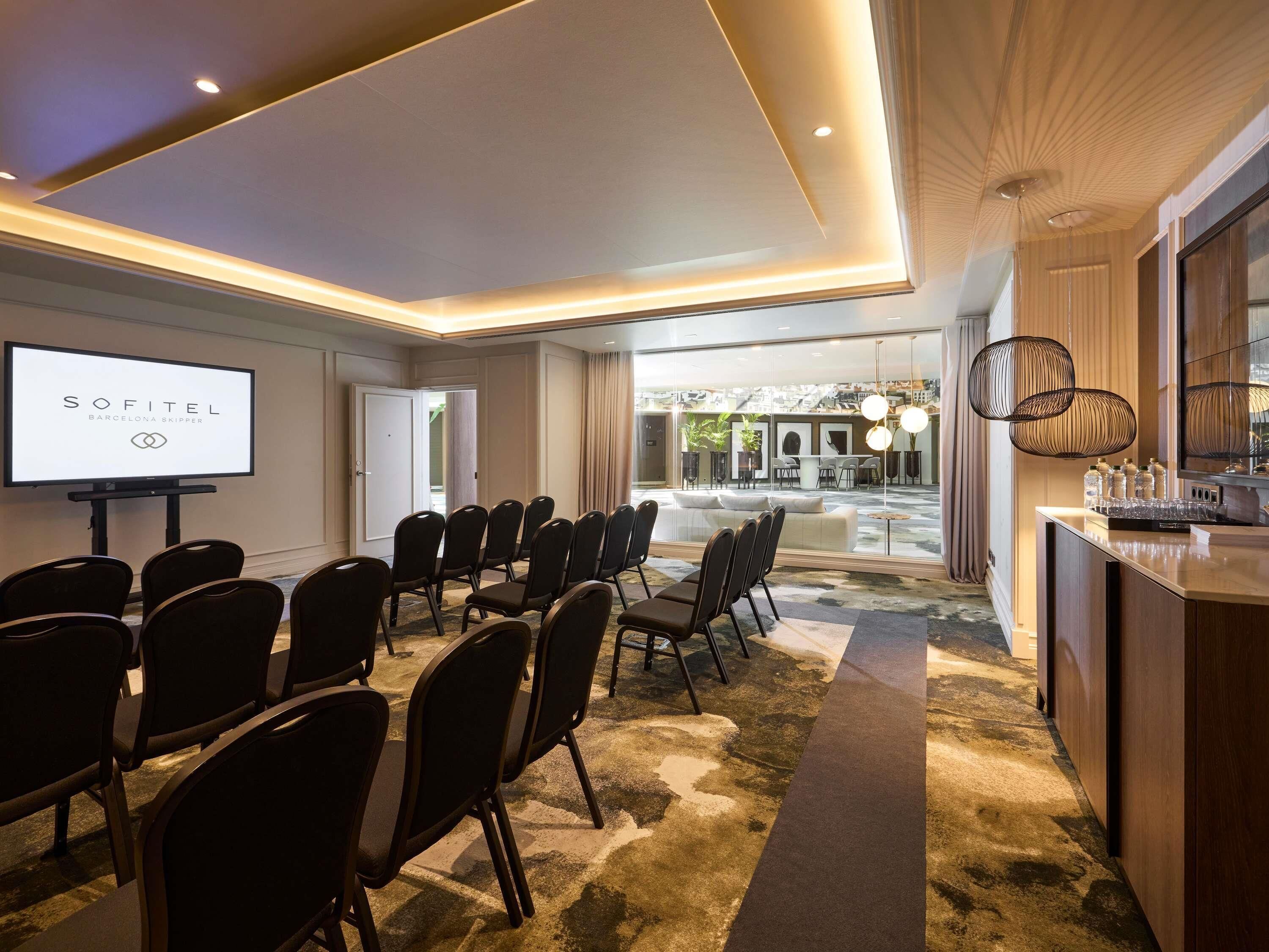 Een vergaderzaal met een projectiescherm, rijen stoelen, een bar en uitzicht op de buitenruimte.