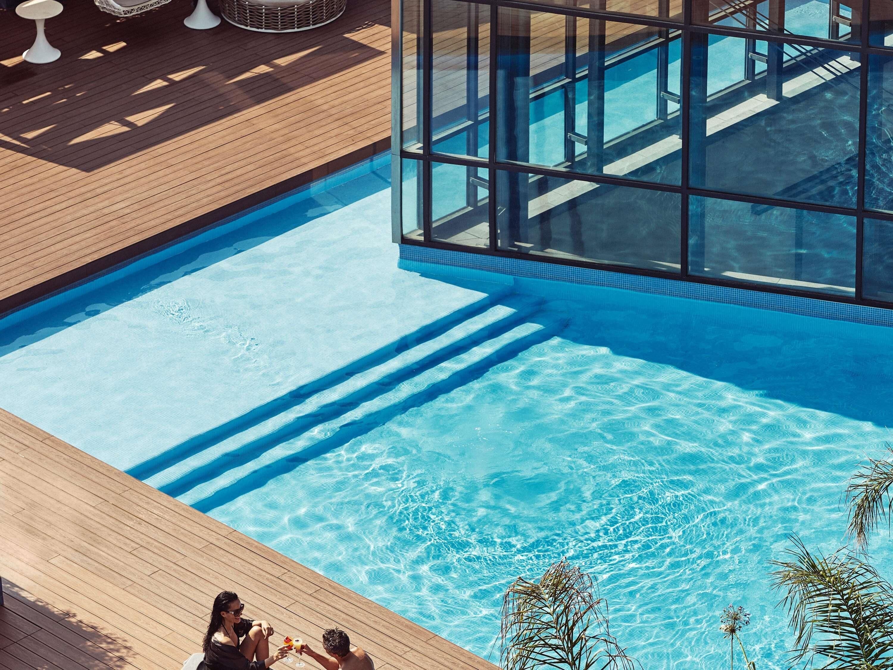 Une piscine à l’eau d’un bleu cristallin, avec une terrasse en bois et des parois en verre.
