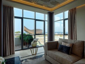 Un salon moderne avec un canapé, une petite table d’appoint et une vue sur la mer grâce à de grandes fenêtres.