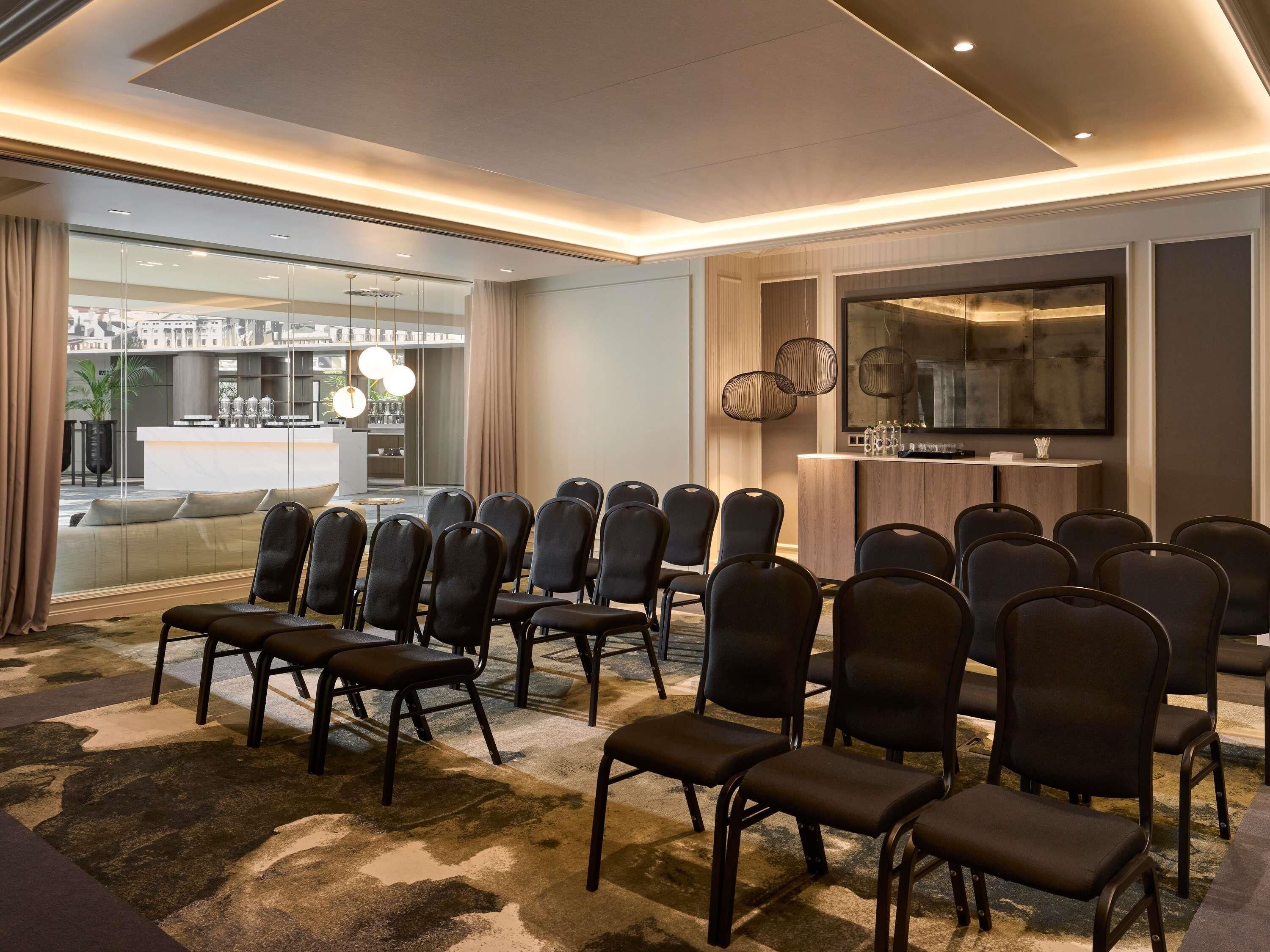 Ett konferensrum med modern design, inrett med ett långt bord och stolar, en bardisk och ett stort fönster med utsikt över stadsbilden.