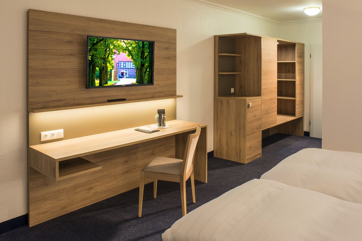 A hotel room with a wooden desk, a TV mounted above it, a bed, and built-in shelving.