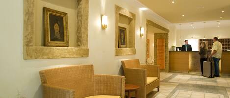 A reception area with wicker furniture, framed portraits on the walls, and a reception desk.