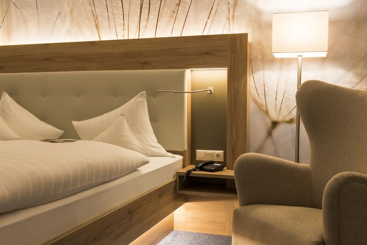 A neatly arranged hotel room with a bed, bedside table, lamp, and chair.