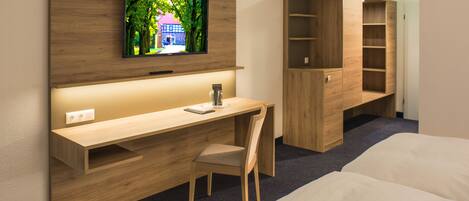Una habitación de hotel moderna con un escritorio de madera, un televisor montado en la pared, una cama y estanterías empotradas.