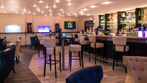 A bar area with multiple seating options, a television mounted on the wall, and a well-stocked bar counter.