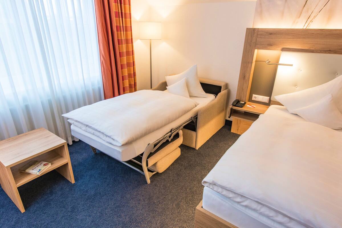 Une chambre d’hôtel avec un lit, une table de chevet, une lampe et une fenêtre avec des rideaux.