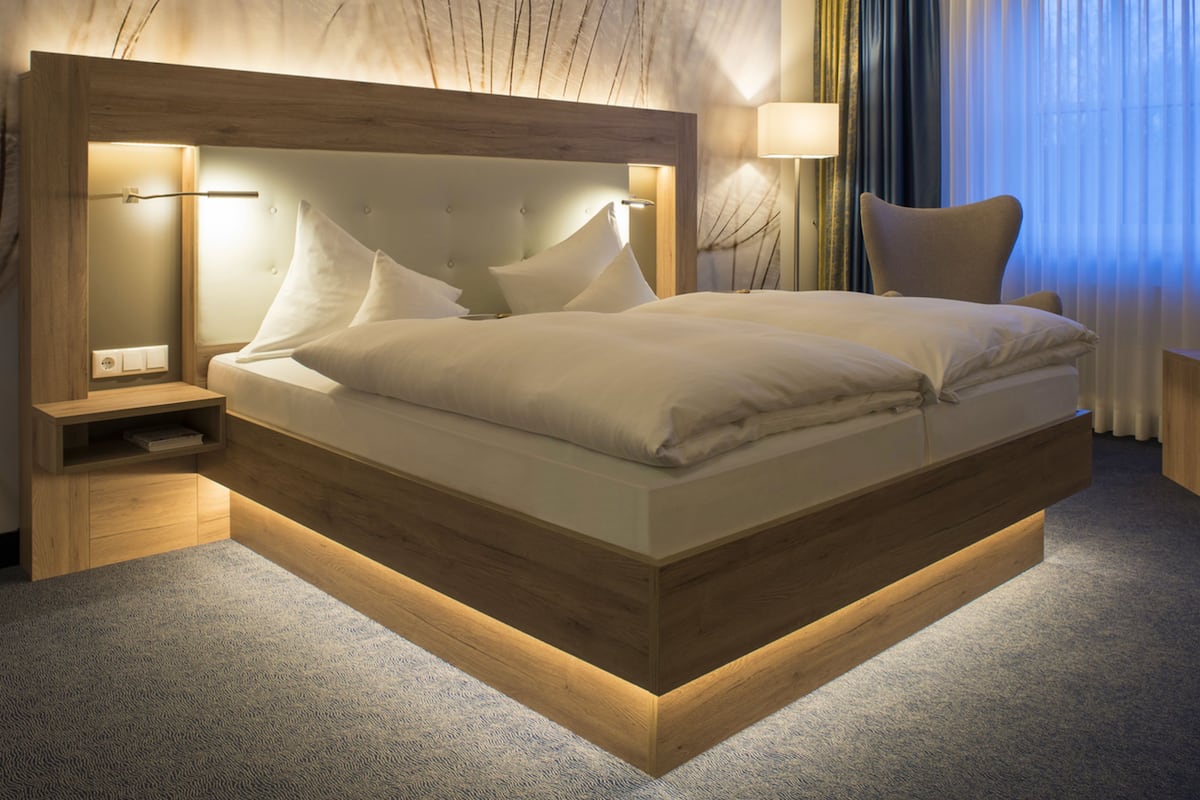 Une chambre d’hôtel moderne avec un grand lit, des tables de chevet, une petite table et une lampe.