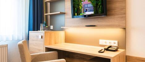 Habitación de hotel con escritorio de madera, un sillón cómodo, televisor de pantalla plana montado en la pared y teléfono integrado.