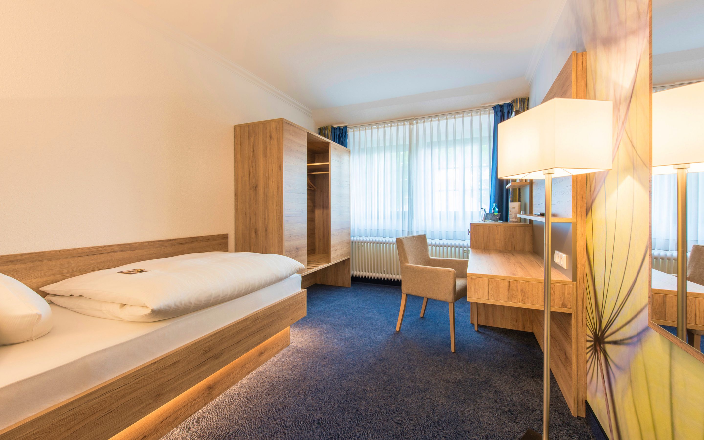 Una habitación de hotel con cama, escritorio, silla, armario y radiador.