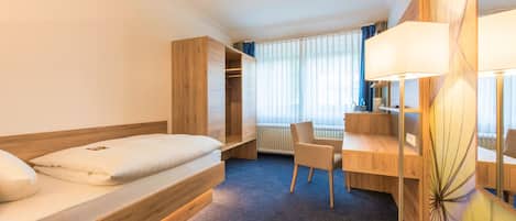 Una habitación de hotel con cama, escritorio, silla, armario y radiador.