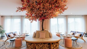 Un amplio salón con una distribución central de asientos, rodeado de sofás y mesas, y un gran árbol artificial en el centro.