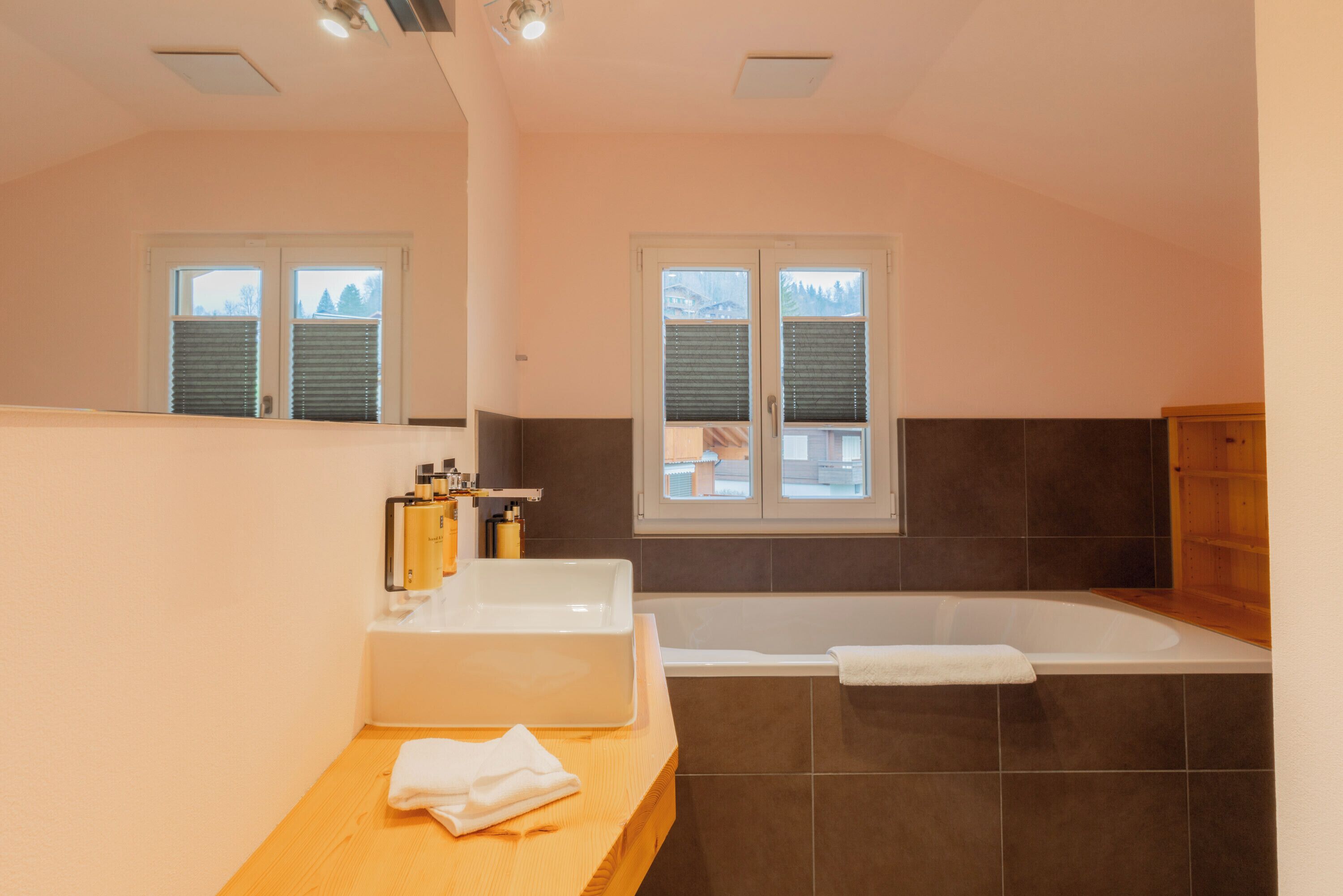 A modern bathroom with a bathtub, a sink, and a window with blinds.