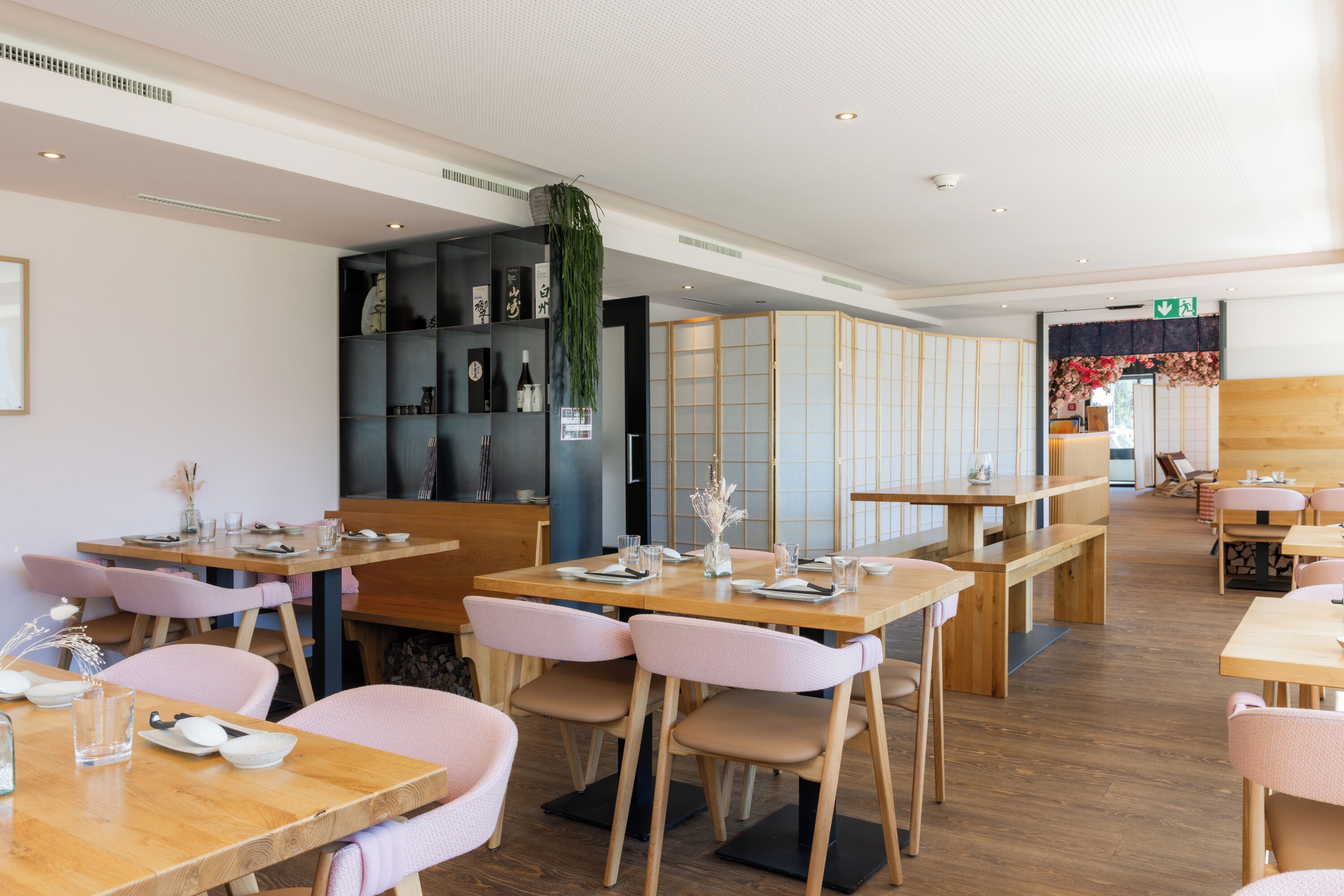 A modern restaurant interior with wooden tables and chairs, a sushi bar, and a traditional Japanese room with tatami flooring.