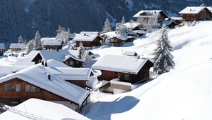 Un pueblo cubierto de nieve con casas de madera, un telesilla y un telón de fondo montañoso.