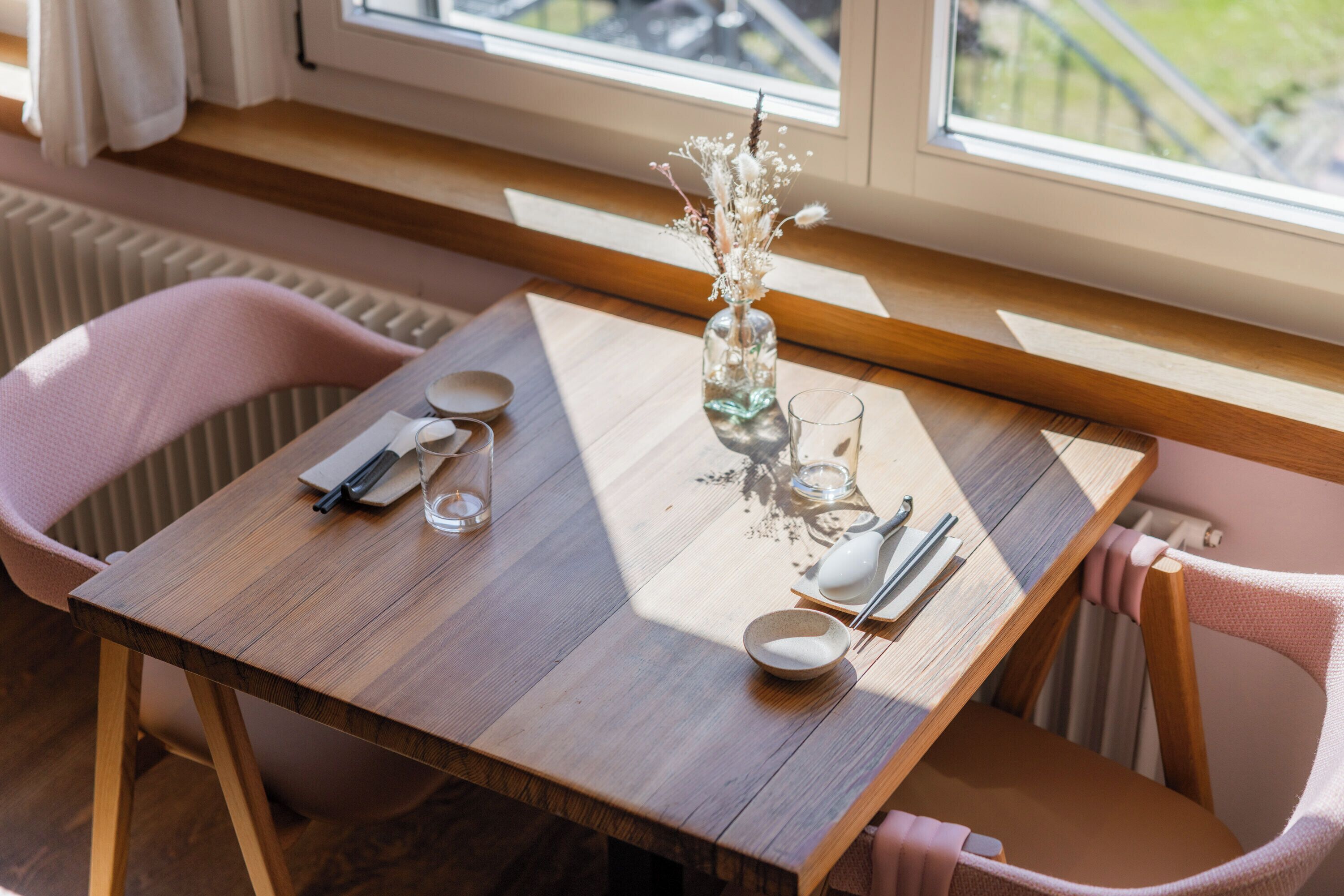Een houten eettafel met een bloemetjesvaas, een glas en bestek.