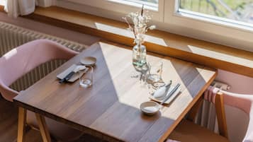 Een houten eettafel met een bloemetjesvaas, een glas en bestek.