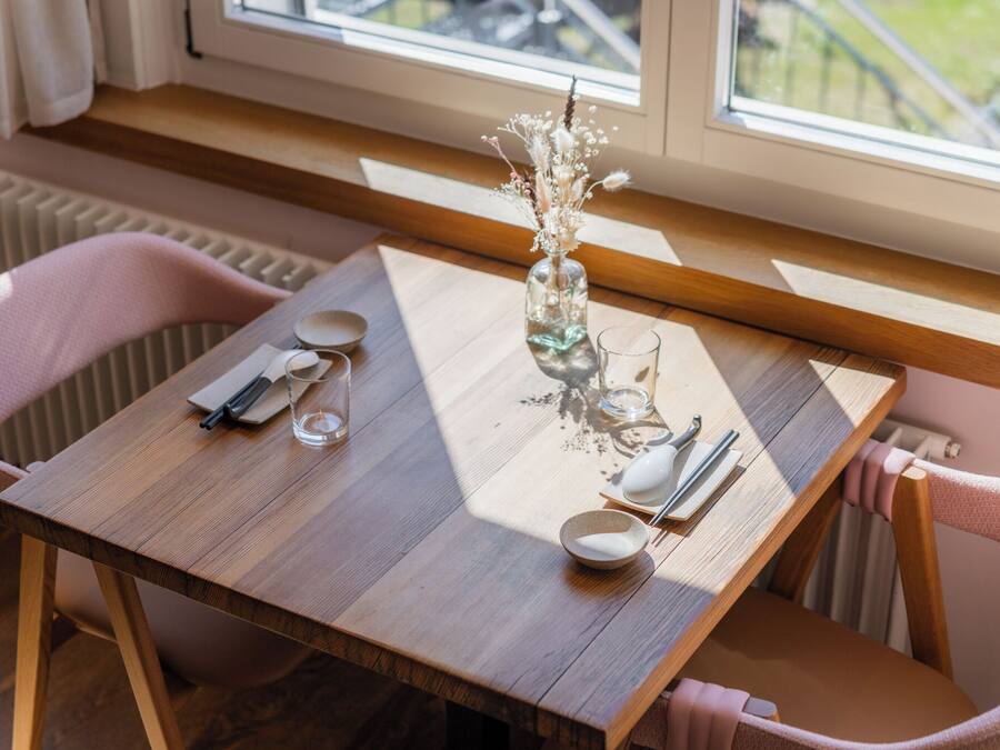Een houten eettafel met een bloemetjesvaas, een glas en bestek.