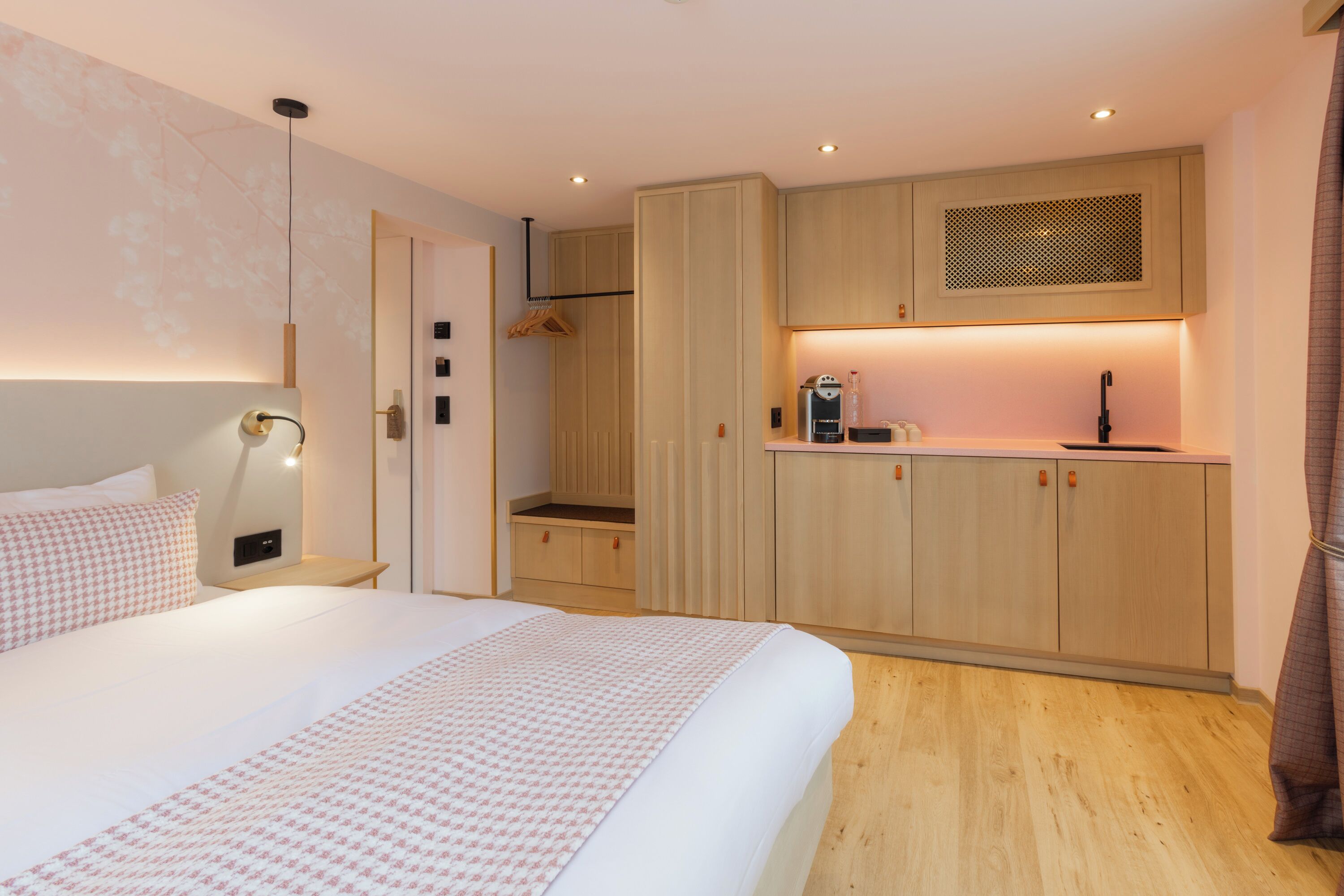 A modern bedroom with a large bed, a bedside table, a wardrobe, and a kitchenette area.