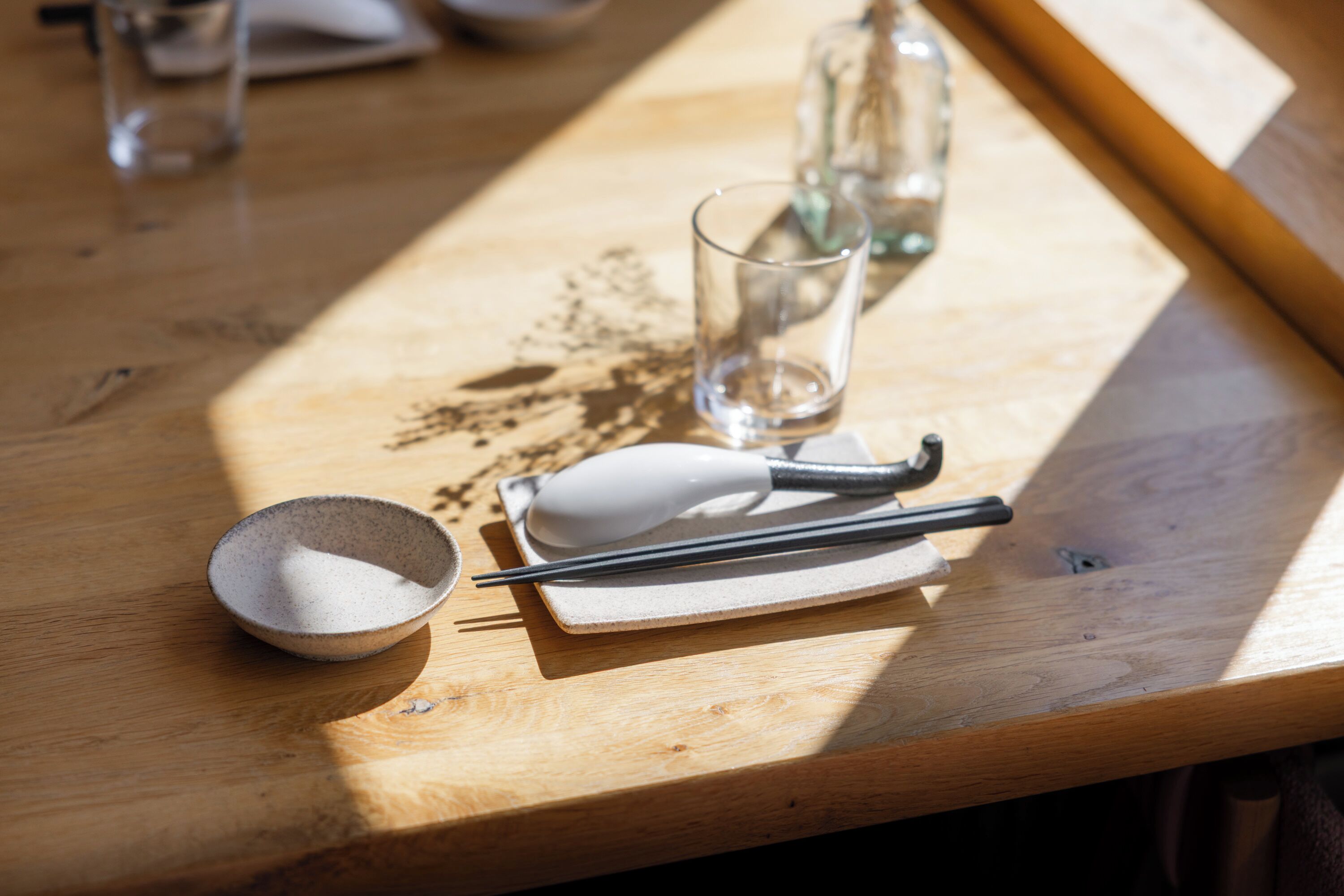 A wooden table with a bowl, chopsticks, a white object, and a glass.