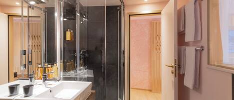 Un baño moderno con ducha envuelta en vidrio, un lavabo grande con dos cubetas y un mueble de tocador de madera.