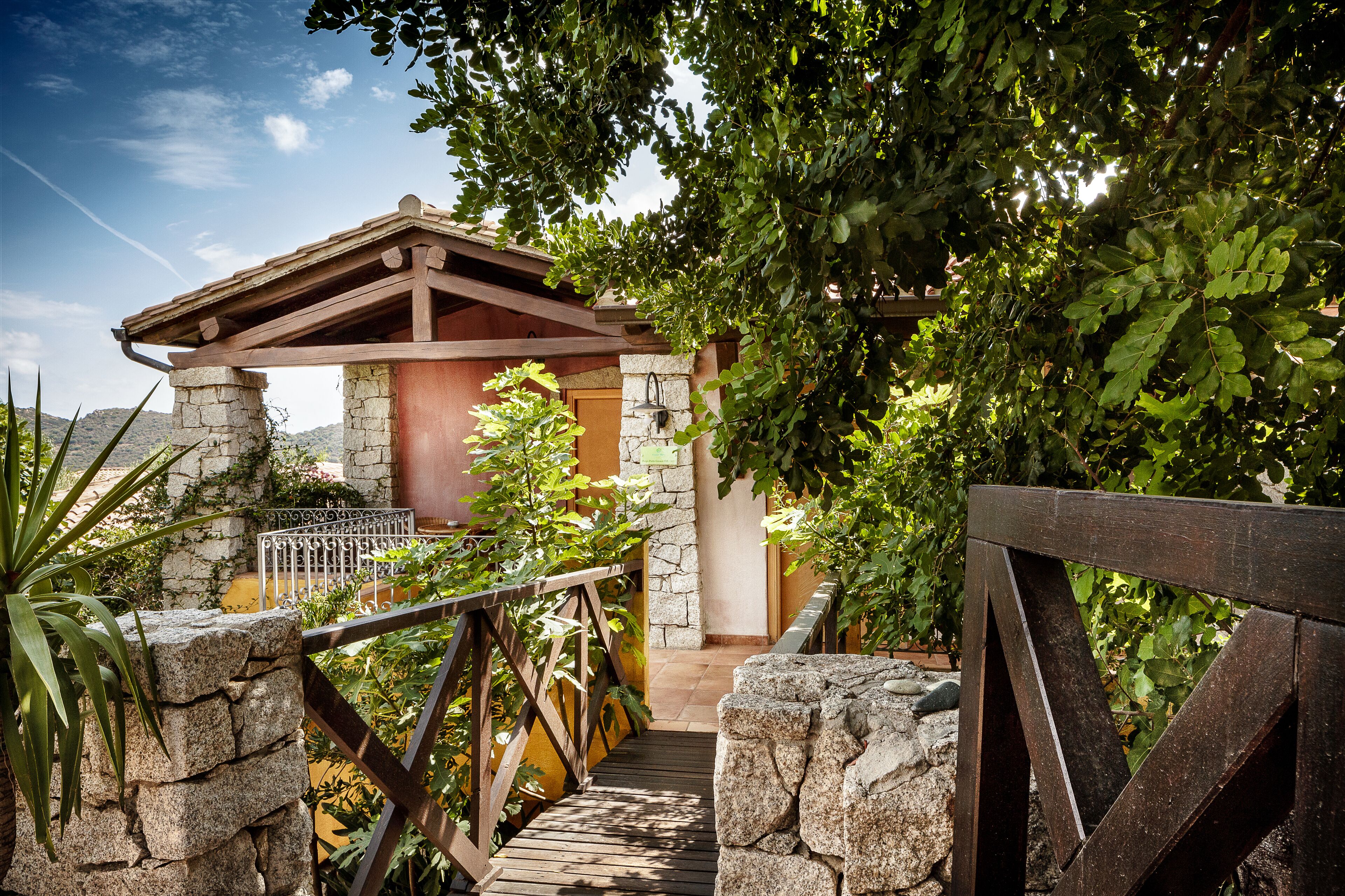 A stone pathway leading to a wooden pergola with a stone wall and a metal railing.