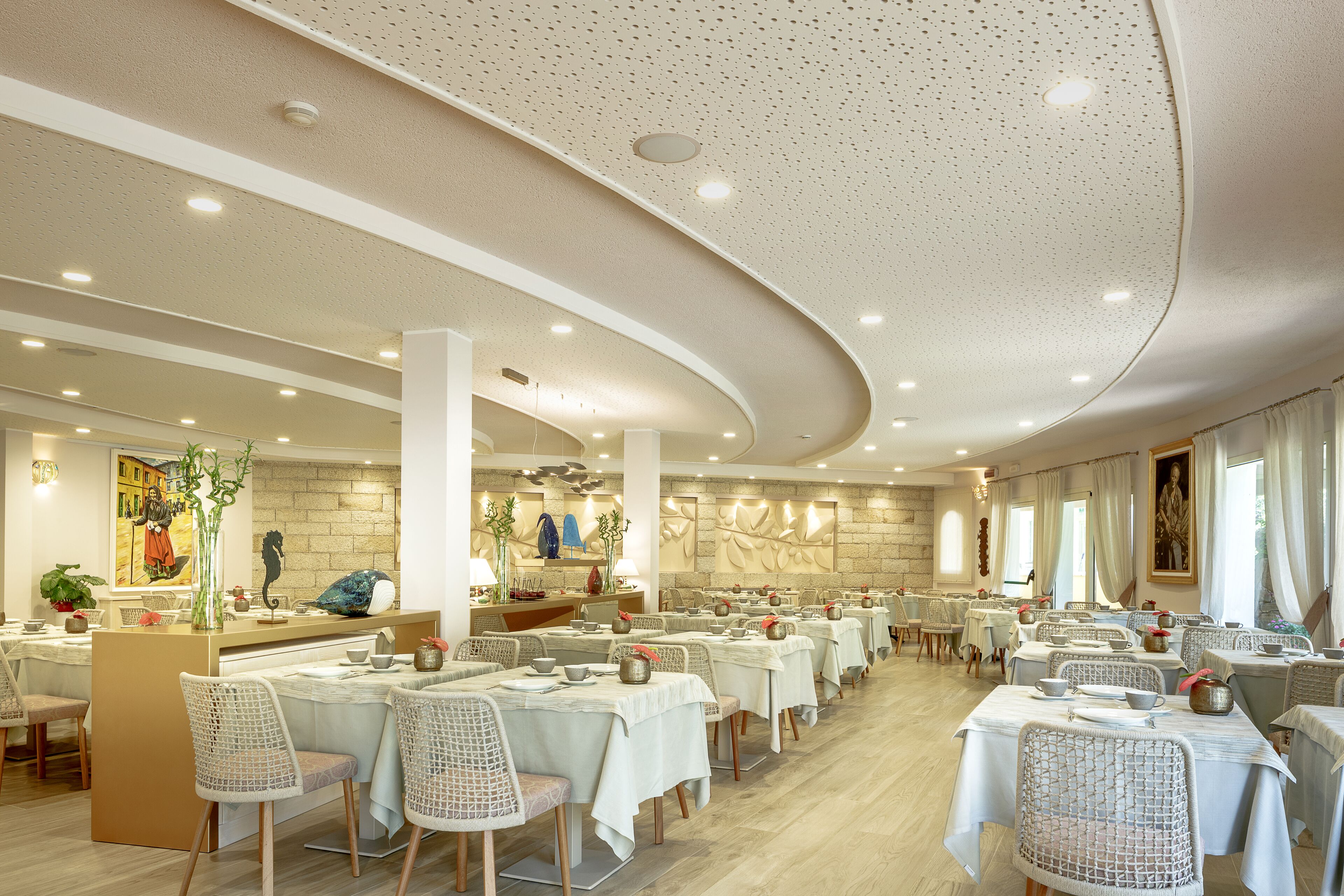 Un comedor amplio con varias mesas y sillas, una isla central con mostrador y una pared decorativa con diseño de piedra.