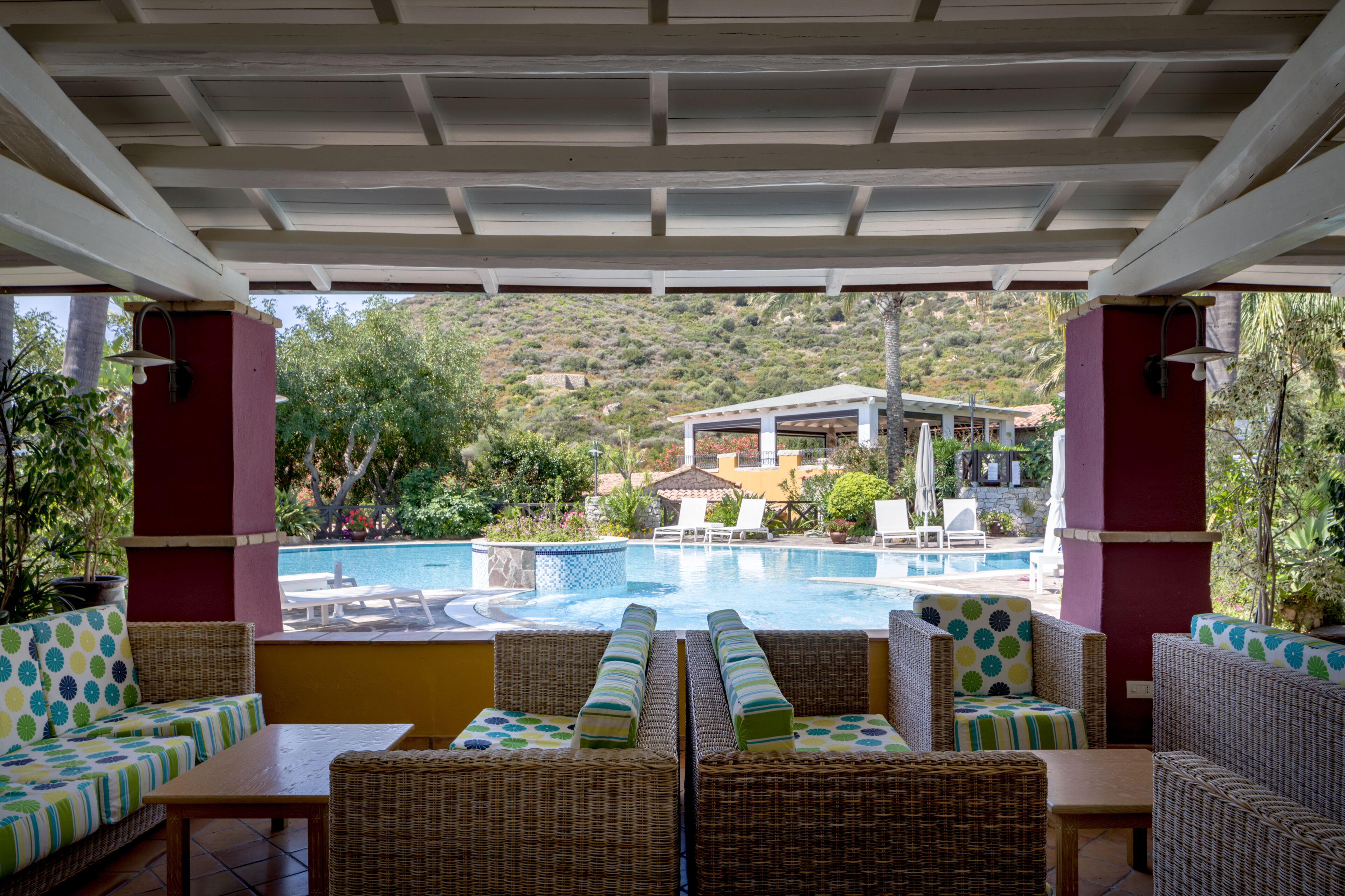 A covered outdoor seating area with wicker furniture, a pool, and a view of a hillside.