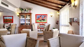 A cozy living room with wicker furniture, a wooden cabinet with glass doors, and framed artwork on the walls.