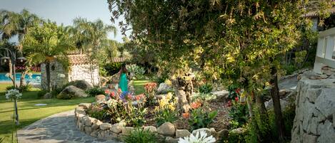 A garden with a stone pathway, various plants, and a stone wall.