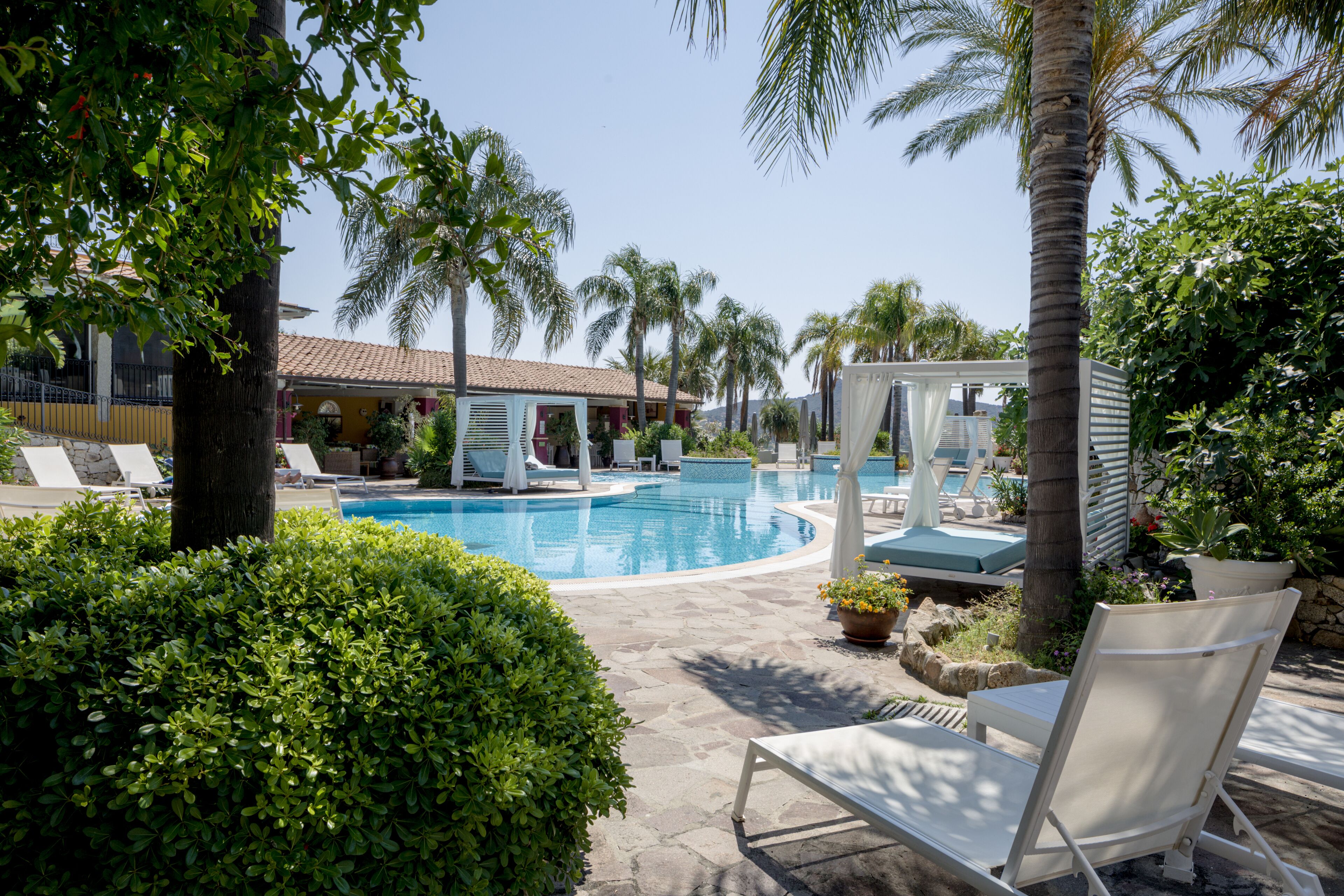 Un espace piscine avec des chaises longues, des palmiers et un bâtiment en arrière-plan.