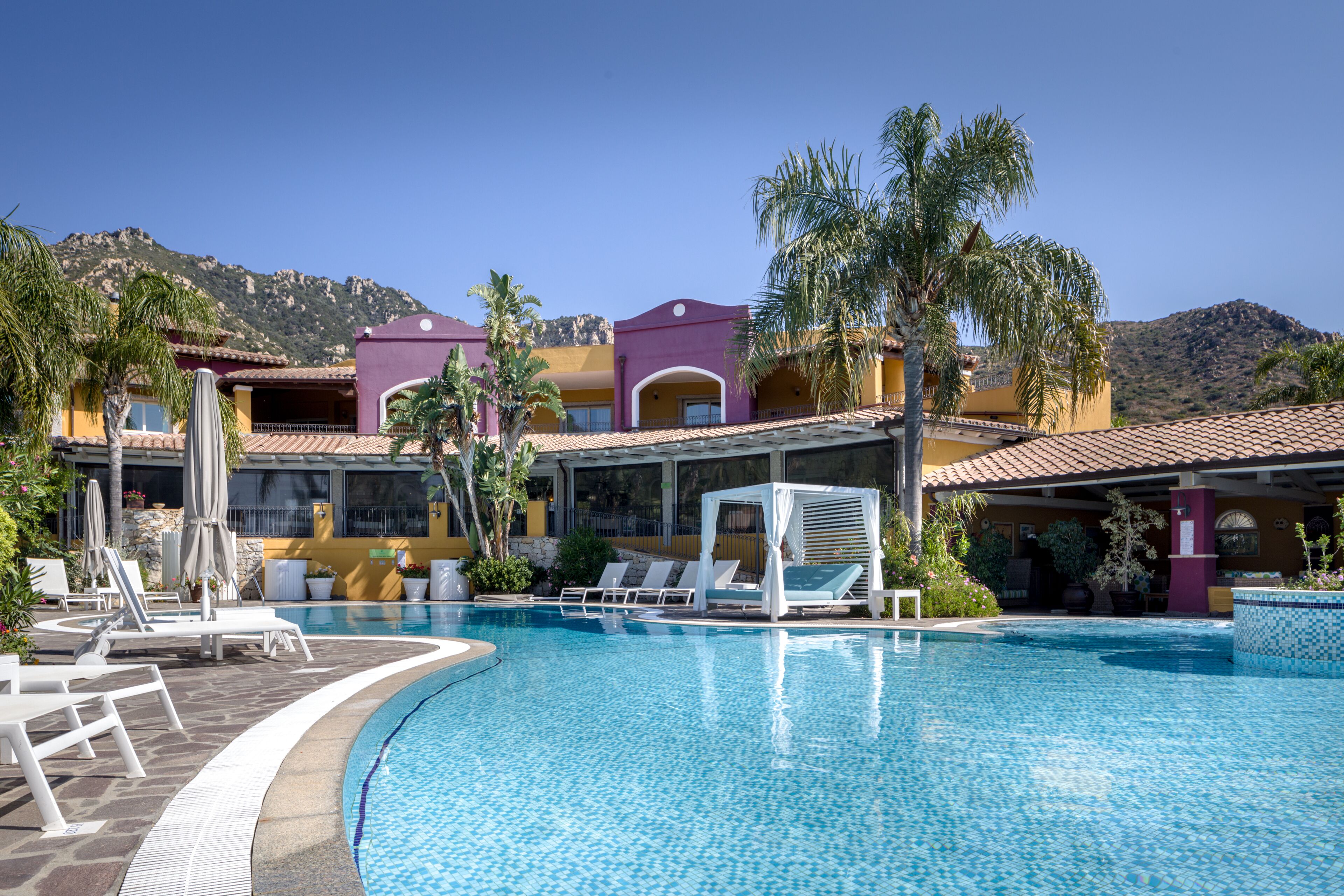 A resort pool area with lounge chairs, a cabana, and a mountain backdrop.