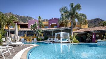 A resort pool area with lounge chairs, a cabana, and a mountain backdrop.