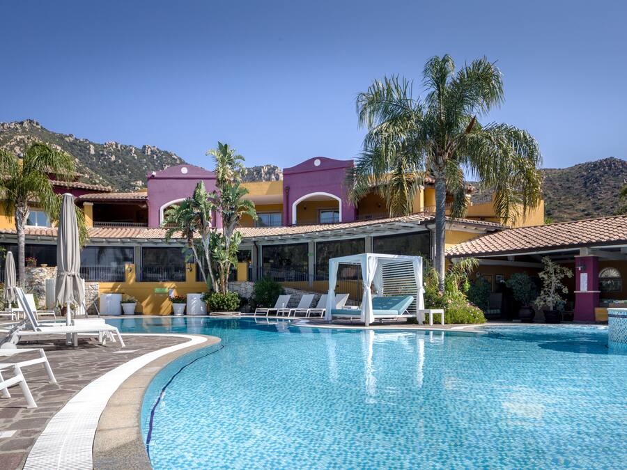 A resort pool area with lounge chairs, a cabana, and a mountain backdrop.