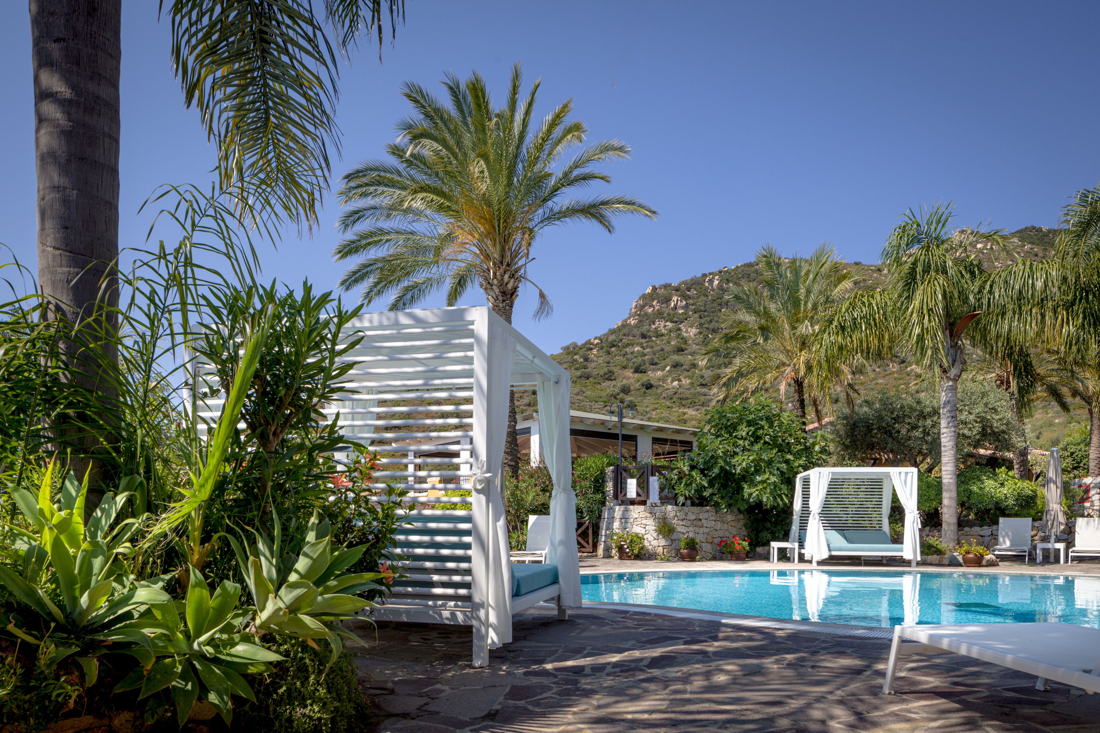 Un espace piscine agrémenté d’un gazebo blanc, de chaises longues et de palmiers.