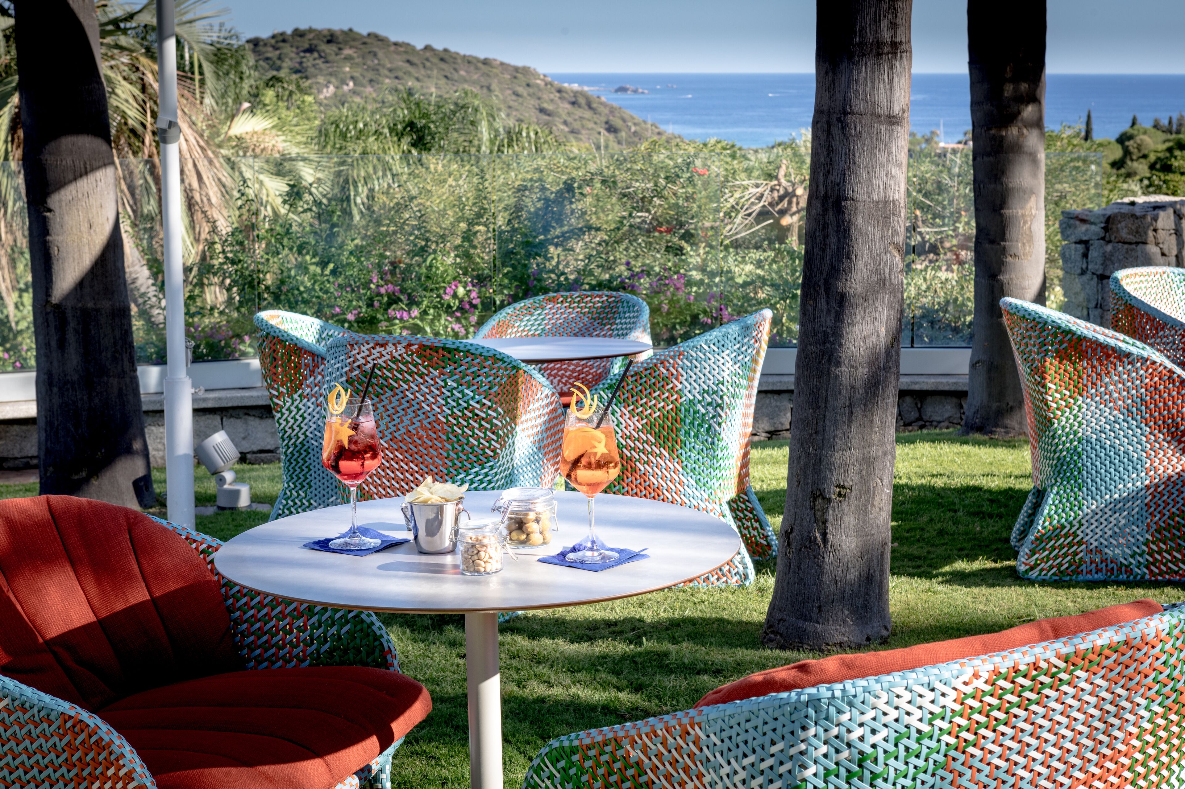A dining area with wicker chairs and a table, overlooking a scenic coastal view.