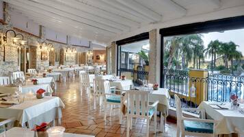 A restaurant with white tables and chairs, stone walls, and a view of palm trees.