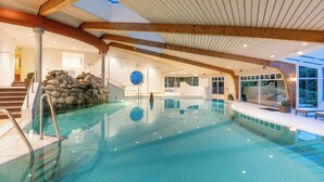 Una piscina interior con agua cristalina, vigas de madera y una pared de piedra.
