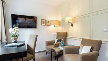 A hotel room with a dining table, two armchairs, a sofa, a TV, and a lamp.