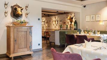 A restaurant with wooden furniture, a wooden cabinet, and a wall decorated with animal skulls and framed pictures.