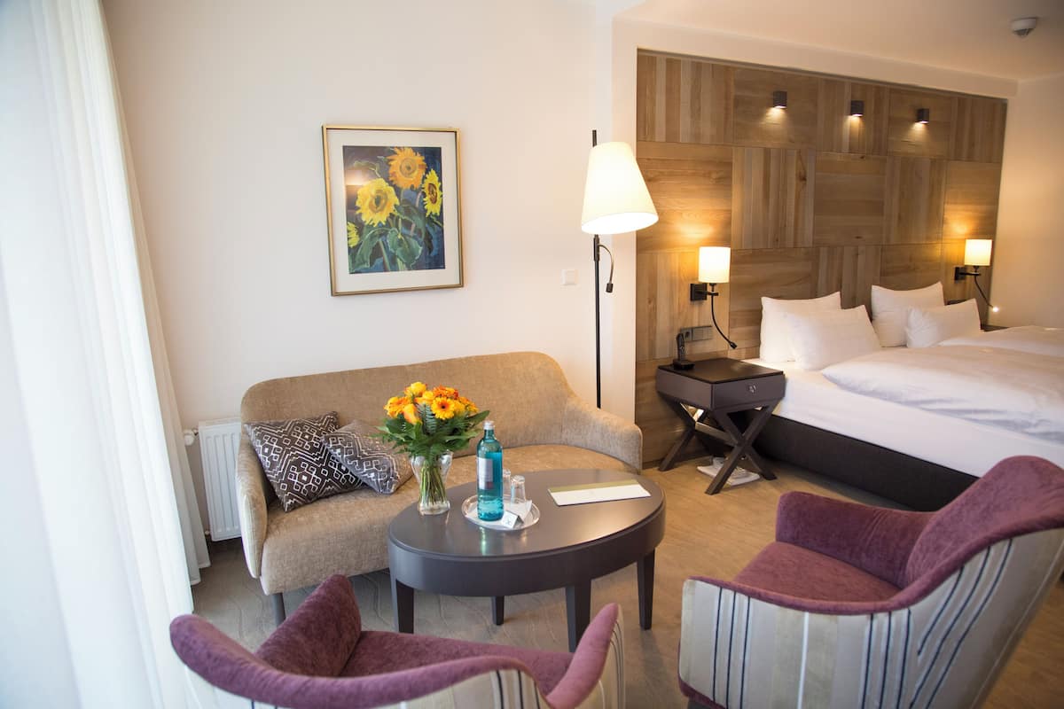 A hotel room with a bed, a sofa, a round coffee table, and two armchairs.