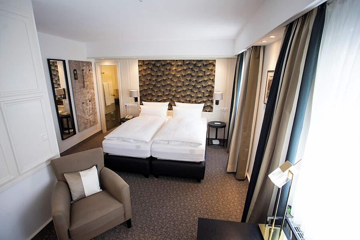 A hotel room with a double bed, a sofa, a small table, and a wall with a textured pattern.